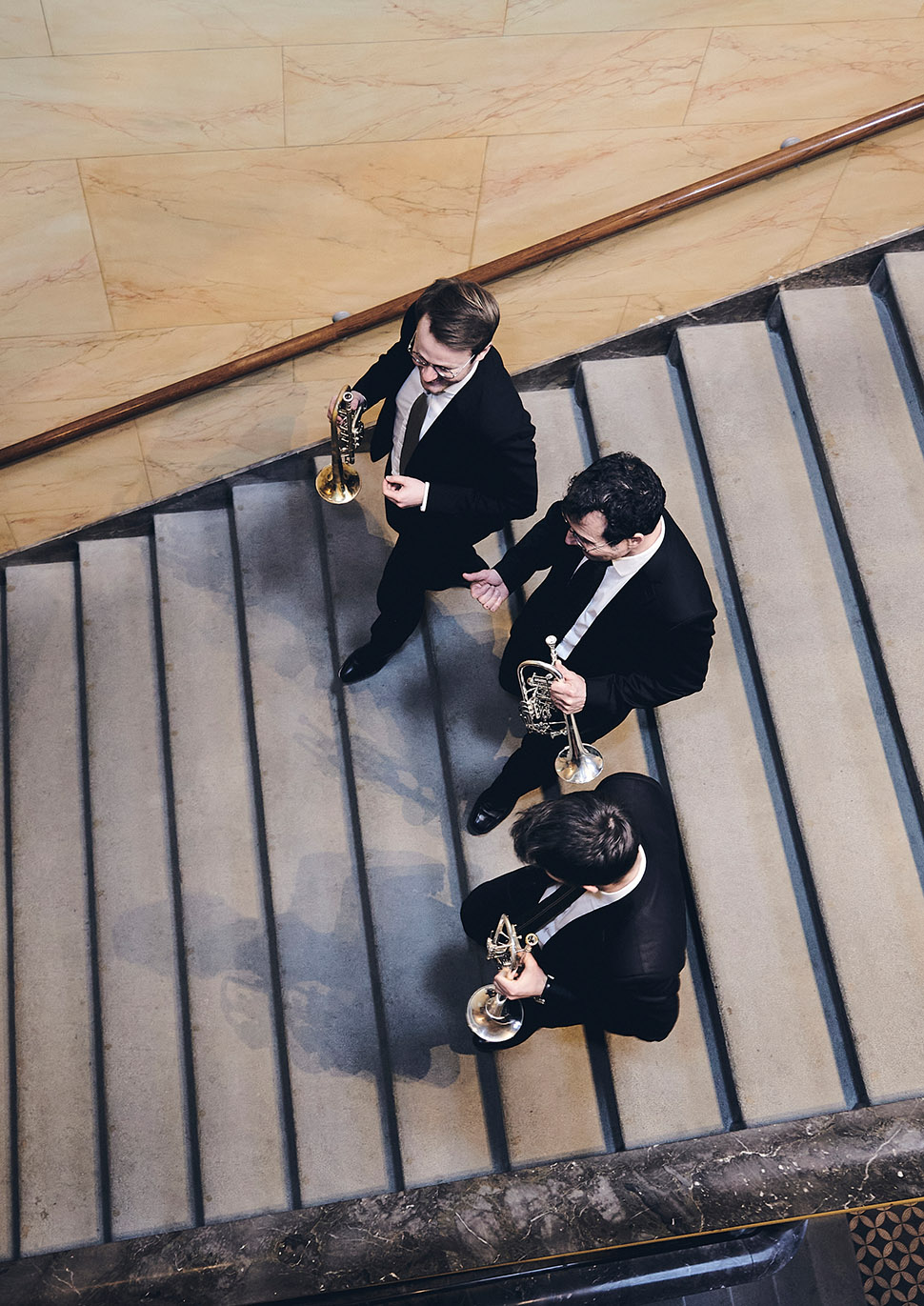 Drei Trompeter, die mit Instrumenten in den Händen eine Treppe hinutergehen